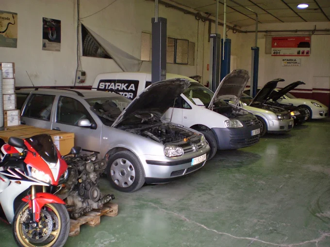 Interior del taller Starka Motor con varios coches y una furgoneta en reparación y una moto en primer plano